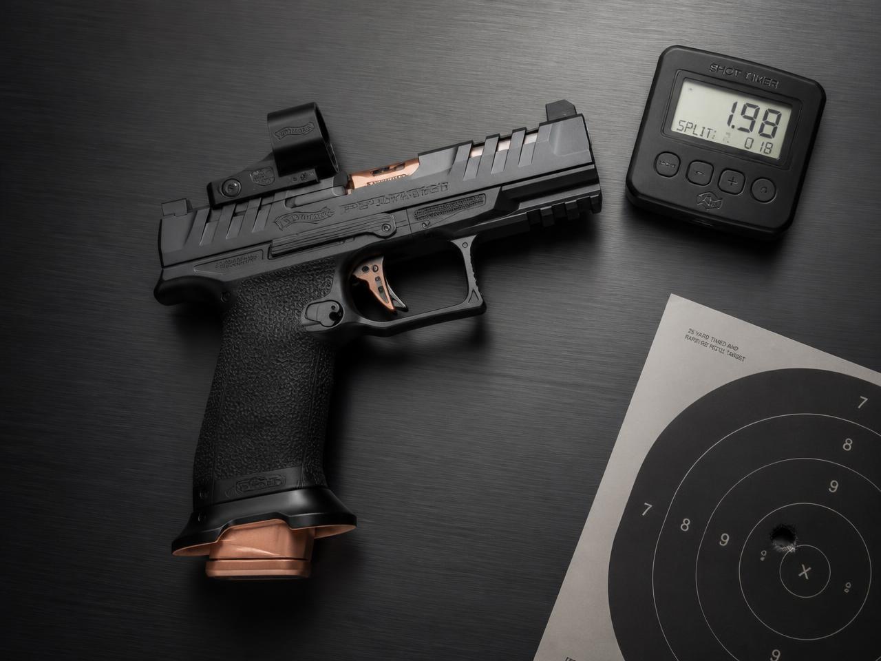 Competition pistol, shot timer and paper target arranged on a graphite surface